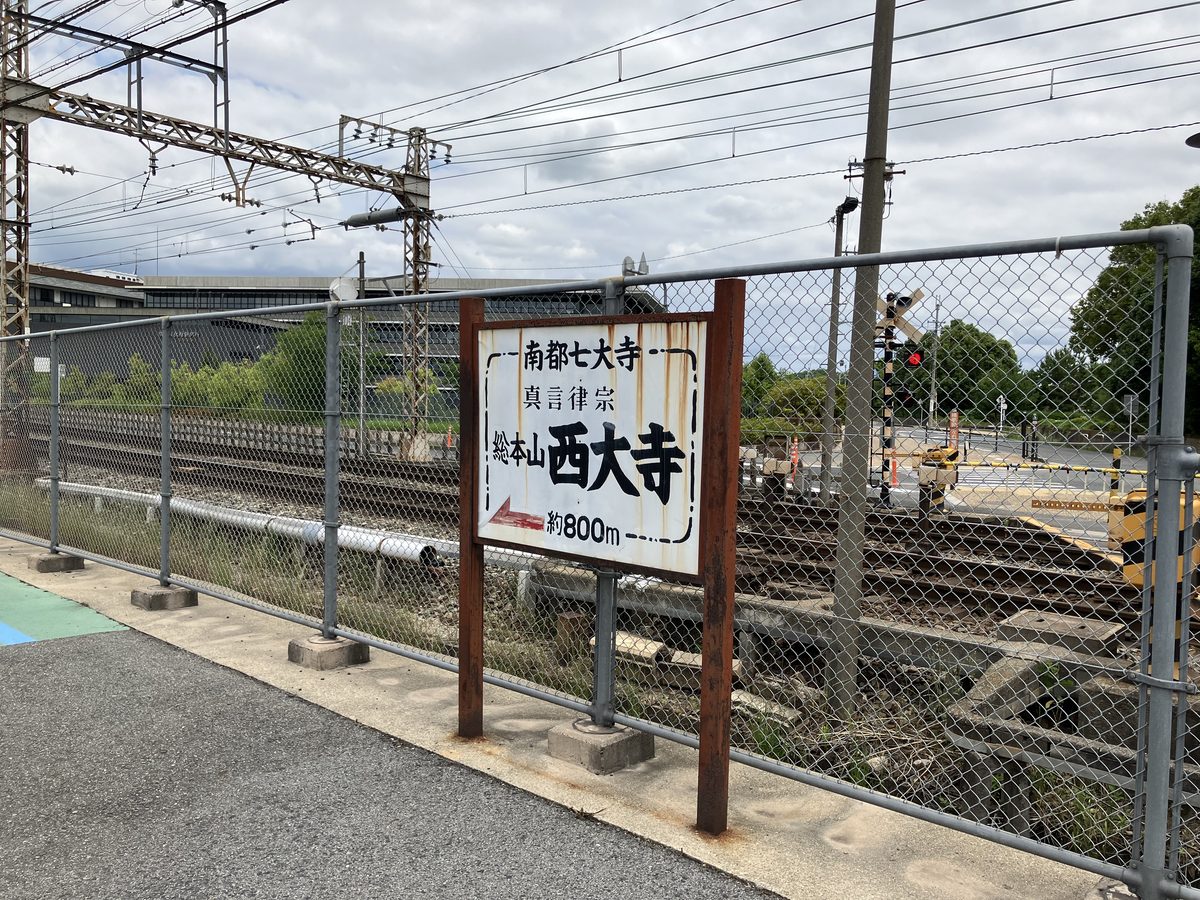 A signboard for Saidaiji Temple visible on the left at the railway crossing
