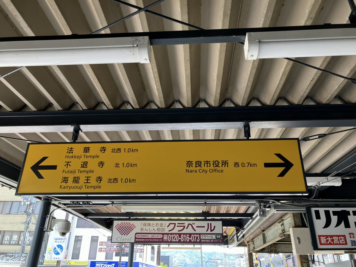 Yellow direction sign inside Shin-Omiya Station showing Nara City Hall to the west